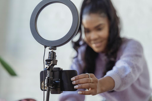 A girl setting up her phone camera on a tripod stand with a ring light to probably shoot some content.