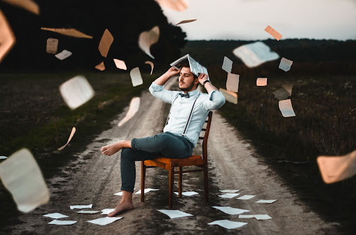 A man on a chair with books and pages flying around, displaying a student.