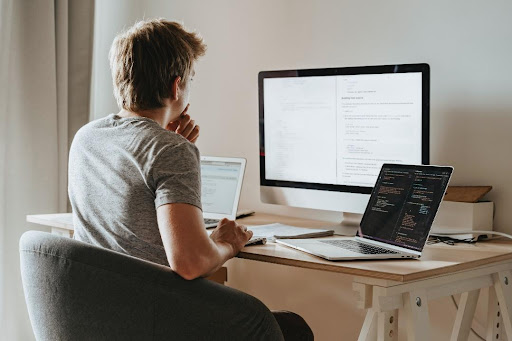 A man sitting and working in front of 3 screens.